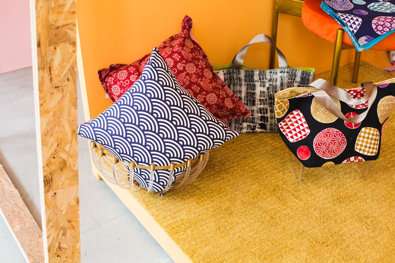 Vibrant decorative pillows and bags in geometric patterns against a colorful indoor backdrop.