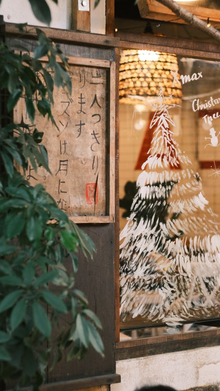 Cozy window display with Christmas tree and festive decorations reflecting a rustic aesthetic.
